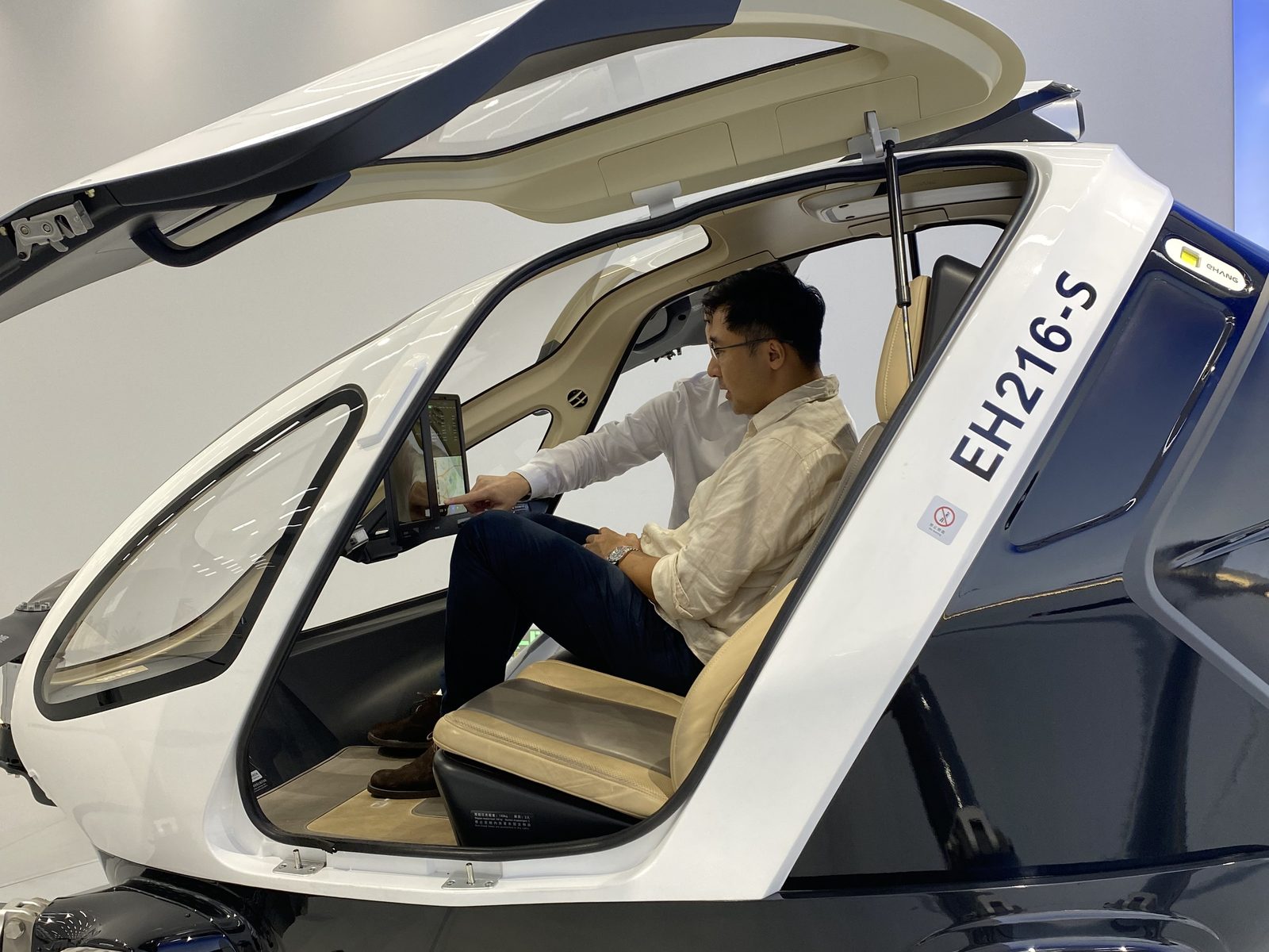 Jason Chan seated inside the EHang EH216-S cabin, pointing at the single tablet interface.