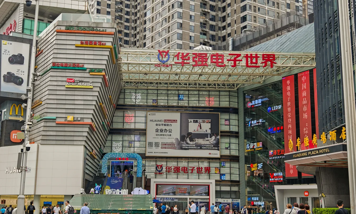 Entrance of the Huaqiangbei electronics world market in Shenzhen, its facade stacked with vendor signs and LED billboards.